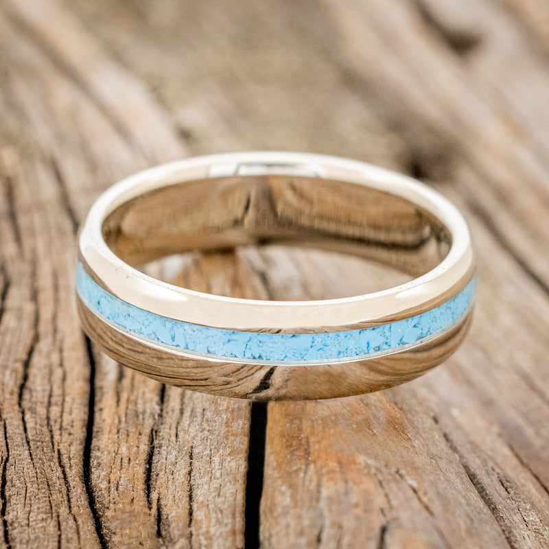 Shown here is "Vertigo", a custom, handcrafted narrow men's wedding ring featuring a turquoise inlay, laying flat. Additional inlay options are available upon request.