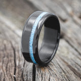 Shown here is "Vertigo", a custom, handcrafted men's wedding ring featuring a turquoise inlay, shown here on a fire-treated black zirconium band, upright facing left. Additional inlay options are available upon request.