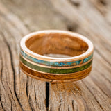 Shown here is "Rio", a custom, handcrafted men's wedding ring featuring 3 channels with patina copper, moss and whiskey barrel oak inlays on a 14K gold band, laying flat. Additional inlay options are available upon request.