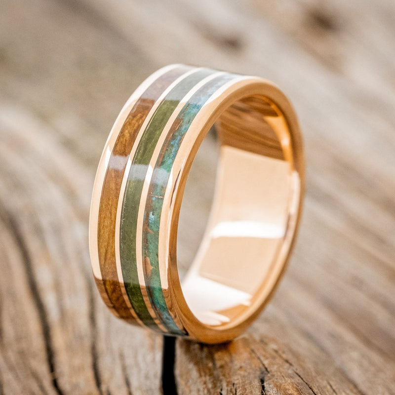 Shown here is "Rio", a custom, handcrafted men's wedding ring featuring 3 channels with patina copper, moss and whiskey barrel oak inlays on a 14K gold band, upright facing left. Additional inlay options are available upon request.