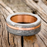Shown here is "Vertigo", a custom, handcrafted hammered men's wedding ring featuring a rustic copper lining and inlay on a fire-treated black zirconium band, laying flat. Additional inlay options are available upon request.
