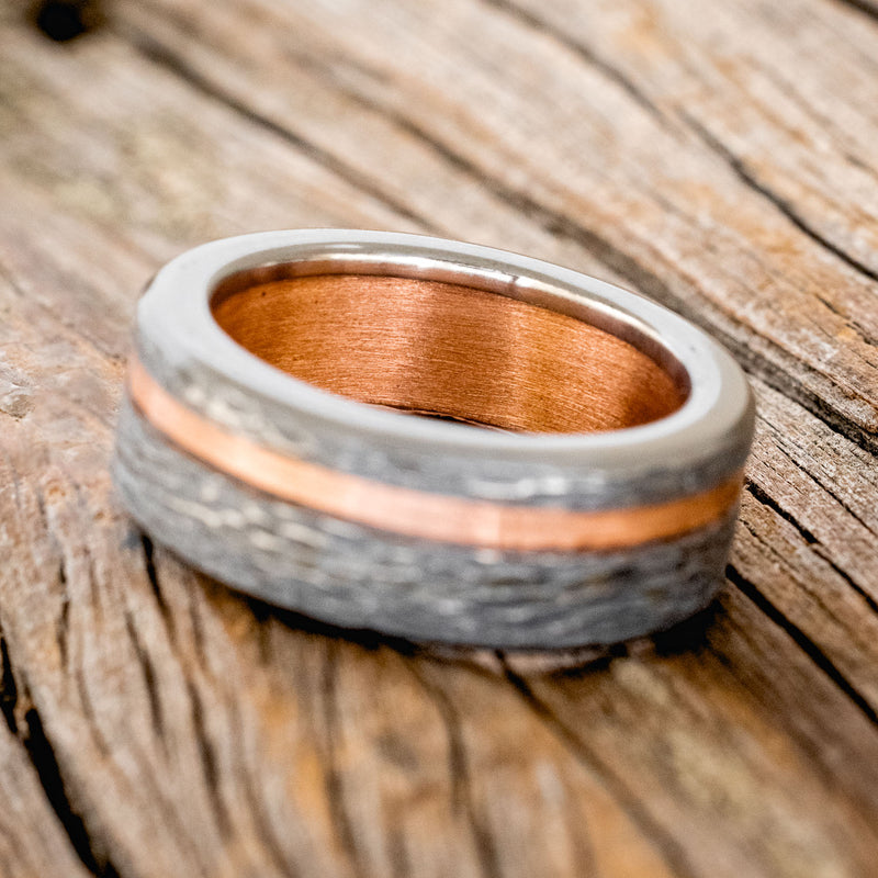 Shown here is "Vertigo", a custom, handcrafted hammered men's wedding ring featuring a rustic copper lining and inlay on a fire-treated black zirconium band, tilted left. Additional inlay options are available upon request.