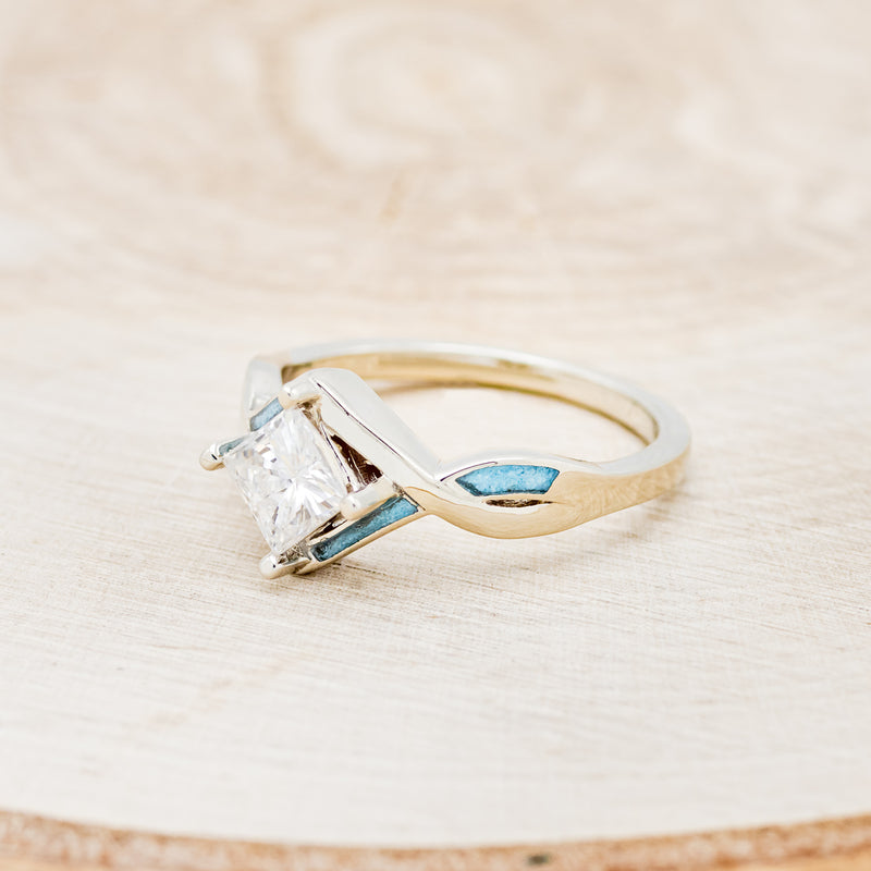 Shown here is "Adamas", a prong-style moissanite women's engagement ring with turquoise inlays, facing left. Many other center stone options are available upon request.