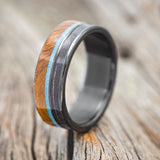 Shown here is "Element", a custom, handcrafted men's wedding ring featuring ironwood, patina copper, and a turquoise inlay on a fire-treated black zirconium band, upright facing left. Additional inlay options are available upon request.