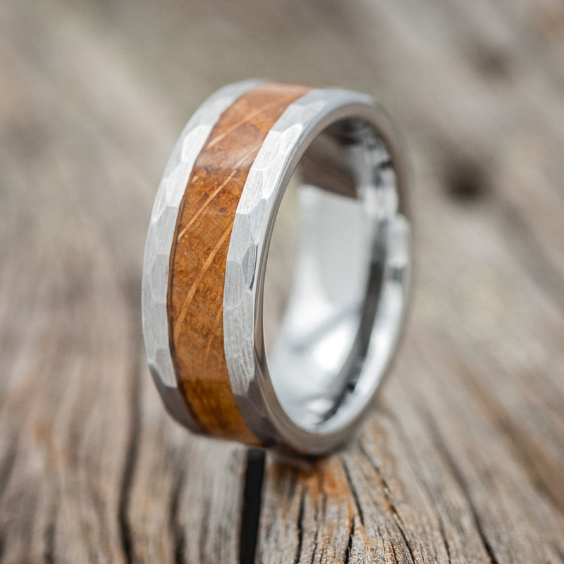 Shown here is a custom, handcrafted men's wedding ring featuring a whiskey barrel inlay on a tungsten band with faceted edges, upright facing left 