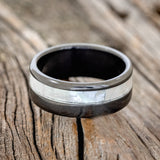 Shown here is "Castor", a custom, handcrafted men's wedding ring featuring a mother of pearl inlay on a fire-treated black zirconium band, laying flat. Additional inlay options are available upon request.