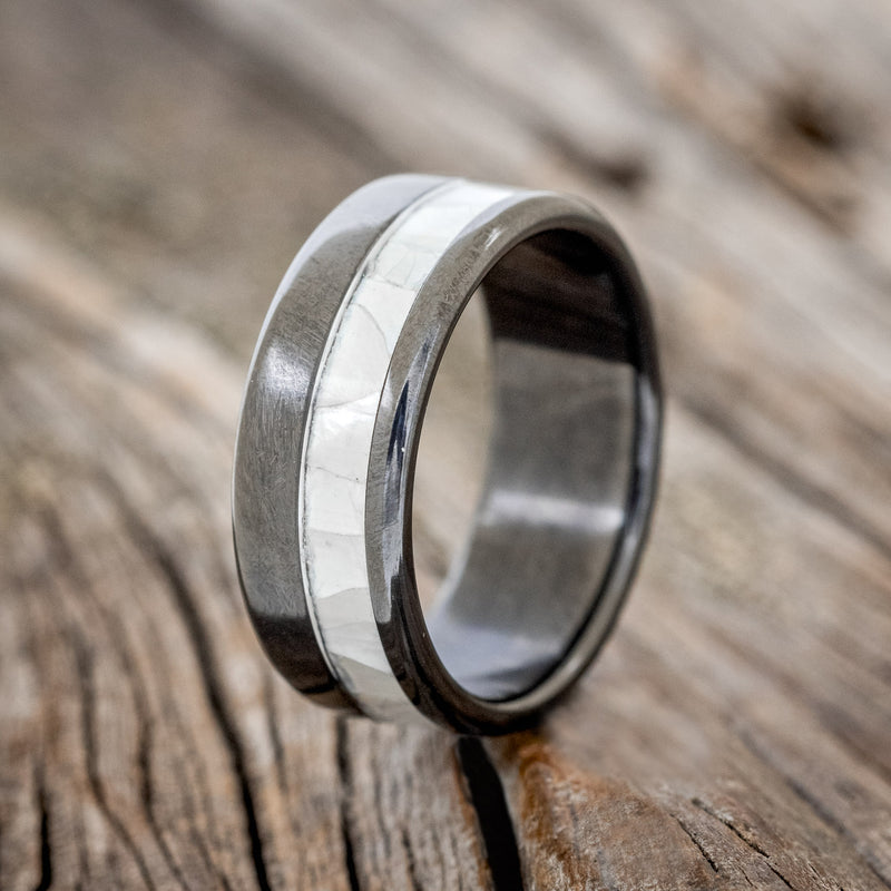 Shown here is "Castor", a custom, handcrafted men's wedding ring featuring a mother of pearl inlay on a fire-treated black zirconium band, upright facing left. Additional inlay options are available upon request.