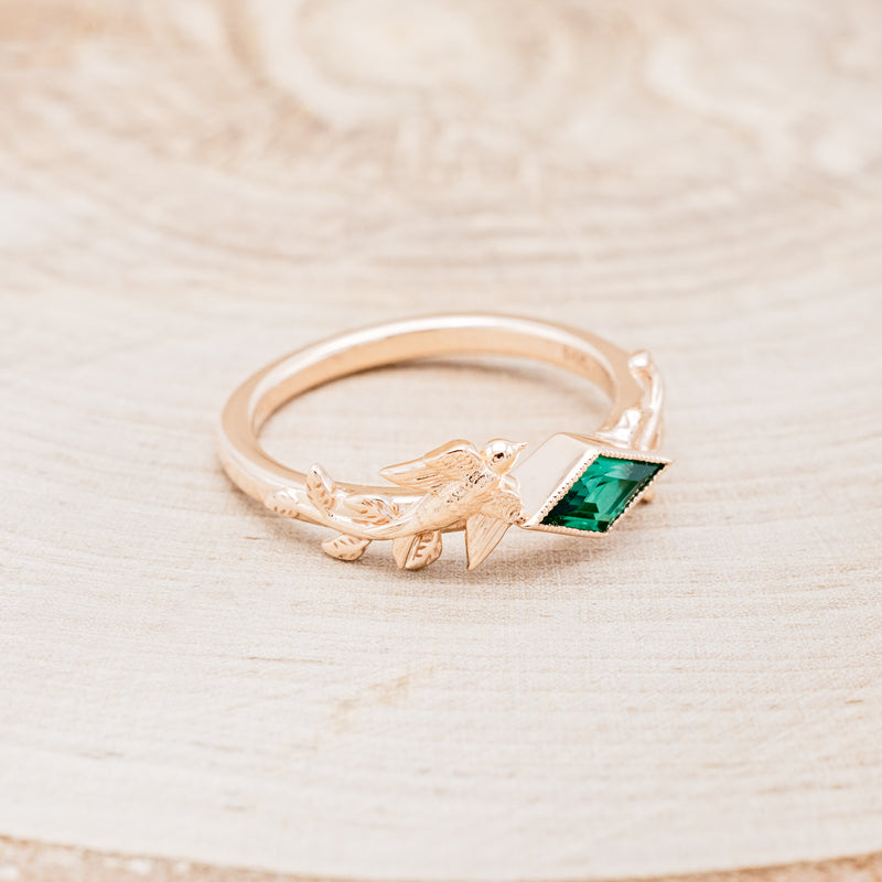 Shown here is "Sparrow", a lab-created emerald women's engagement ring with a sparrow embellishment, facing right. Many other center stone options are available upon request.