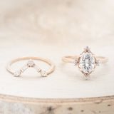 Shown here is "Treva", an oval moissanite women's engagement ring set with diamond accents and a "Melody" tracer, laying flat together. Many other center stone options are available upon request.