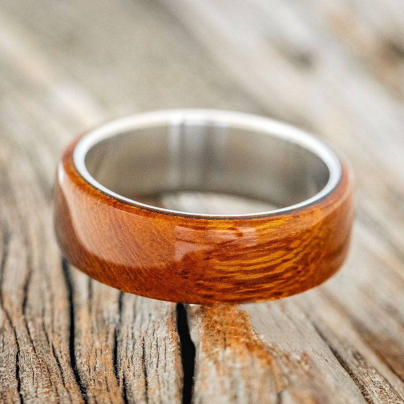 Shown here is "Haven", a custom, handcrafted men's wedding ring featuring an ironwood overlay on a titanium band, laying flat. Additional inlay options are available upon request.