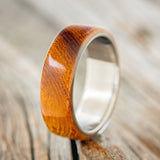 Shown here is "Haven", a custom, handcrafted men's wedding ring featuring an ironwood overlay on a titanium band, upright facing left. Additional inlay options are available upon request.