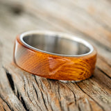 Shown here is "Haven", a custom, handcrafted men's wedding ring featuring an ironwood overlay on a titanium band, tilted left. Additional inlay options are available upon request.