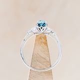 Shown here is "Blossom", a turquoise women's engagement ring with leaf-shaped diamond accents, side view on stand. Many other center stone options are available upon request.