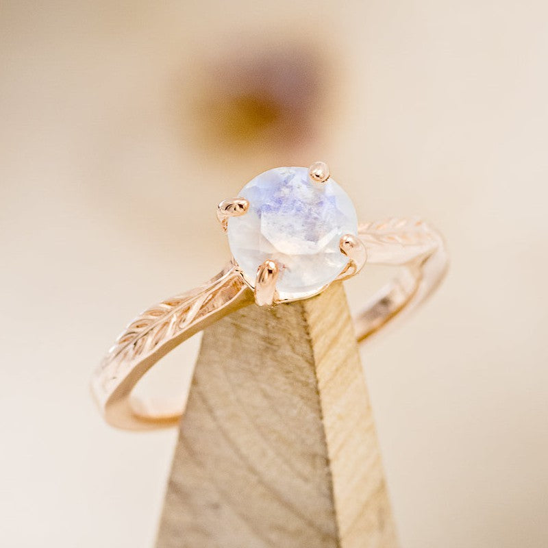 Shown here is "HOPE", a solitaire-style round moonstone women's engagement ring, on stand facing slightly right, with delicate and ornate details and is available with many center stone options