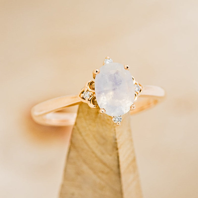 Shown here is "Zella", an accented-style oval moonstone women's engagement ring with diamond accents, on stand facing slightly right. Many other center stone options available upon request.