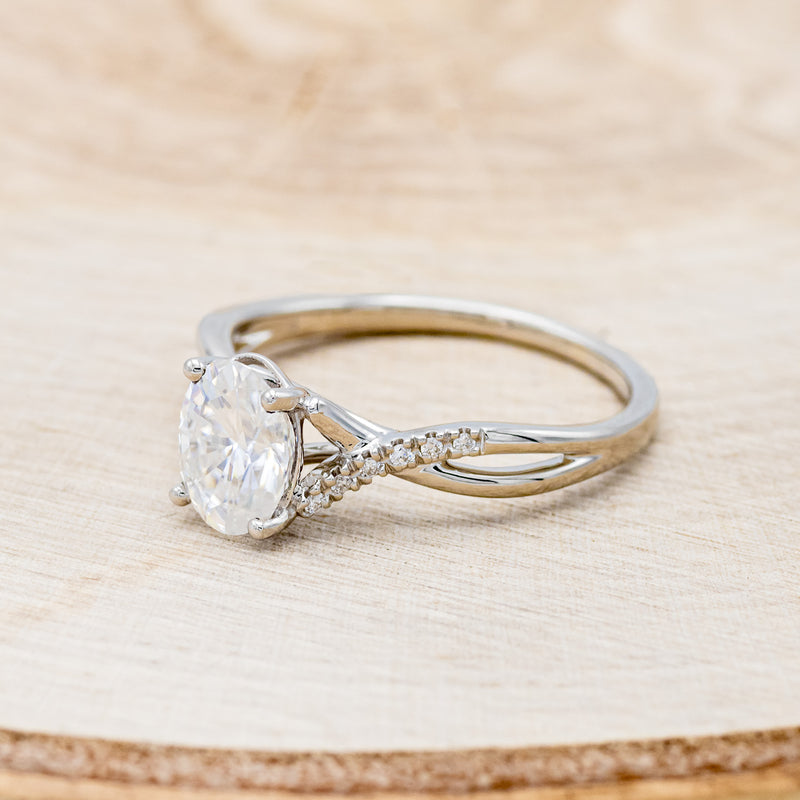 Shown her is "Roslyn", an oval moissanite women's engagement ring with diamond accents, facing left. Many other center stone options are available upon request.