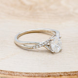Shown her is "Roslyn", an oval moissanite women's engagement ring with diamond accents, facing right. Many other center stone options are available upon request.