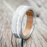 Shown here is "Vertigo", a handcrafted men's wedding ring featuring authentic whiskey barrel oak lining and an elk antler inlay, upright facing left. Shown here set on an etched Damascus steel band. Additional inlay options are available upon request.