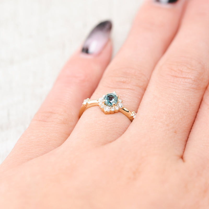 Shown here, the Starla, a round cut denim Montana sapphire women's engagement ring with a starburst diamond halo, on hand. Many other center stone options are available upon request.