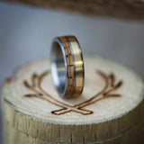 Shown here is "Dyad", a custom, handcrafted men's wedding ring featuring 2 channels with whiskey barrel oak and 14K yellow gold inlays, upright facing right. Additional inlay options are available upon request.